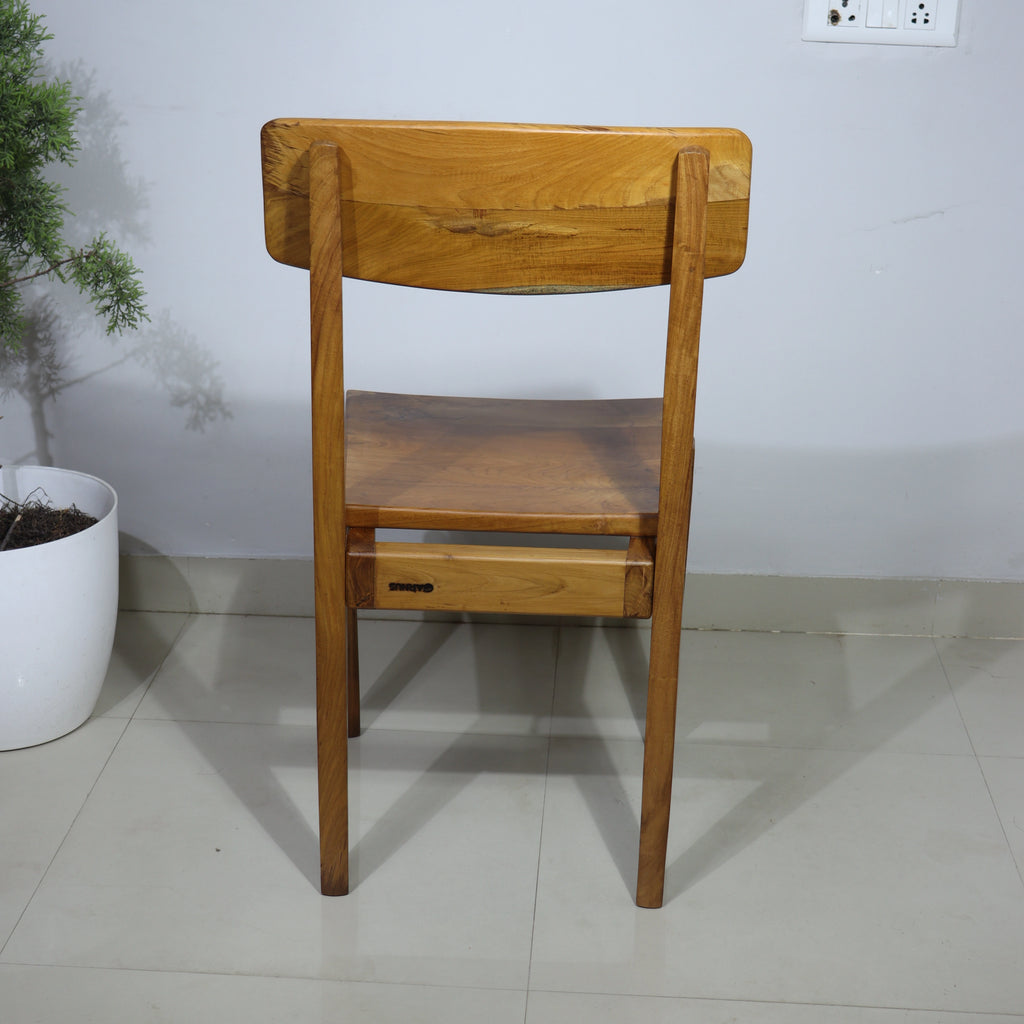 Wooden chair against a plain wall with a plant in the background