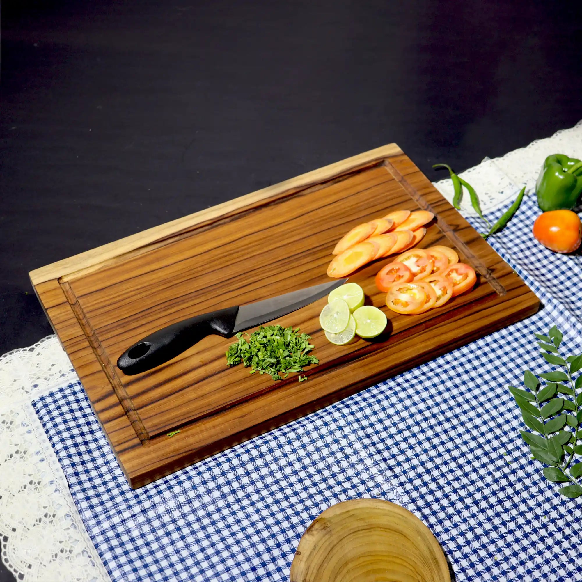 Wooden cutting board with knife and sliced vegetables on a checkered tablecloth