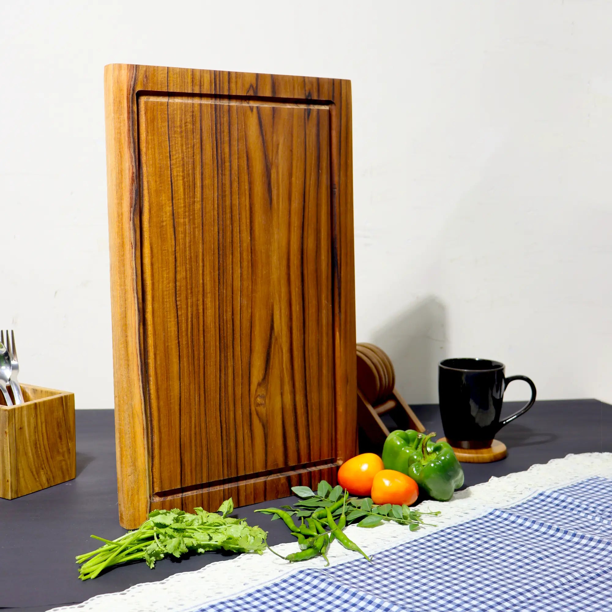 Wooden cutting board with juice groove on a kitchen counter with vegetables and a mug.