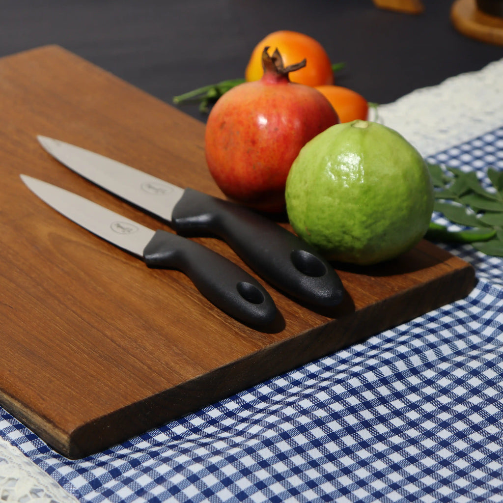 Wooden cutting board with knives, pomegranates, and a lime on a checkered tablecloth.