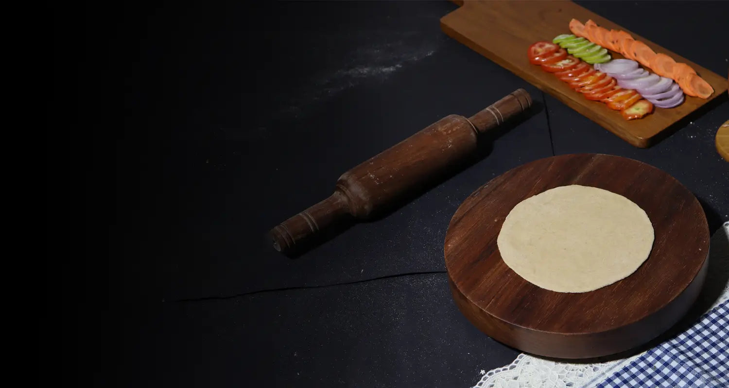 Wooden rolling pin and flatbread on a dark surface with a checkered cloth.