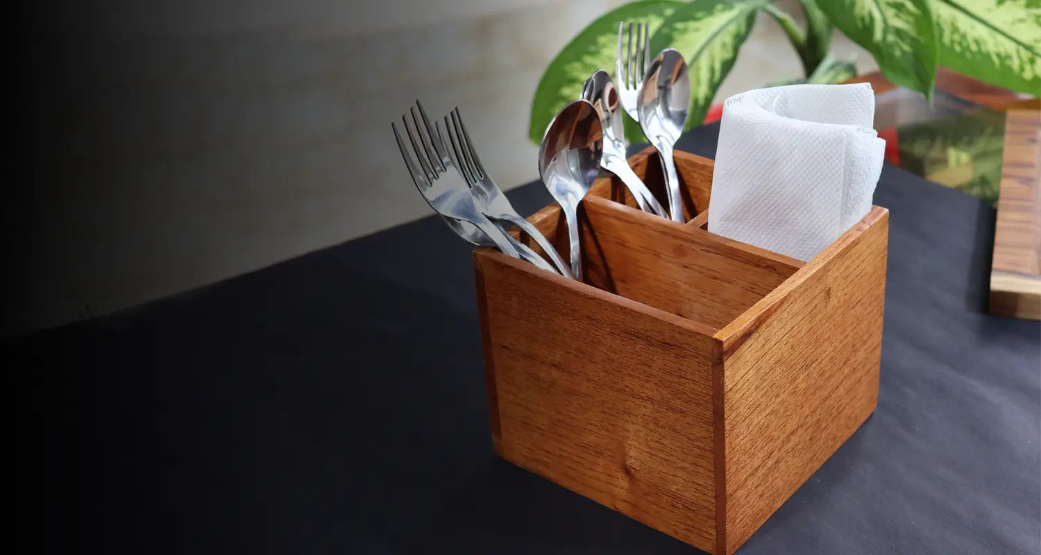 Wooden utensil holder with cutlery and tissues on a dark surface