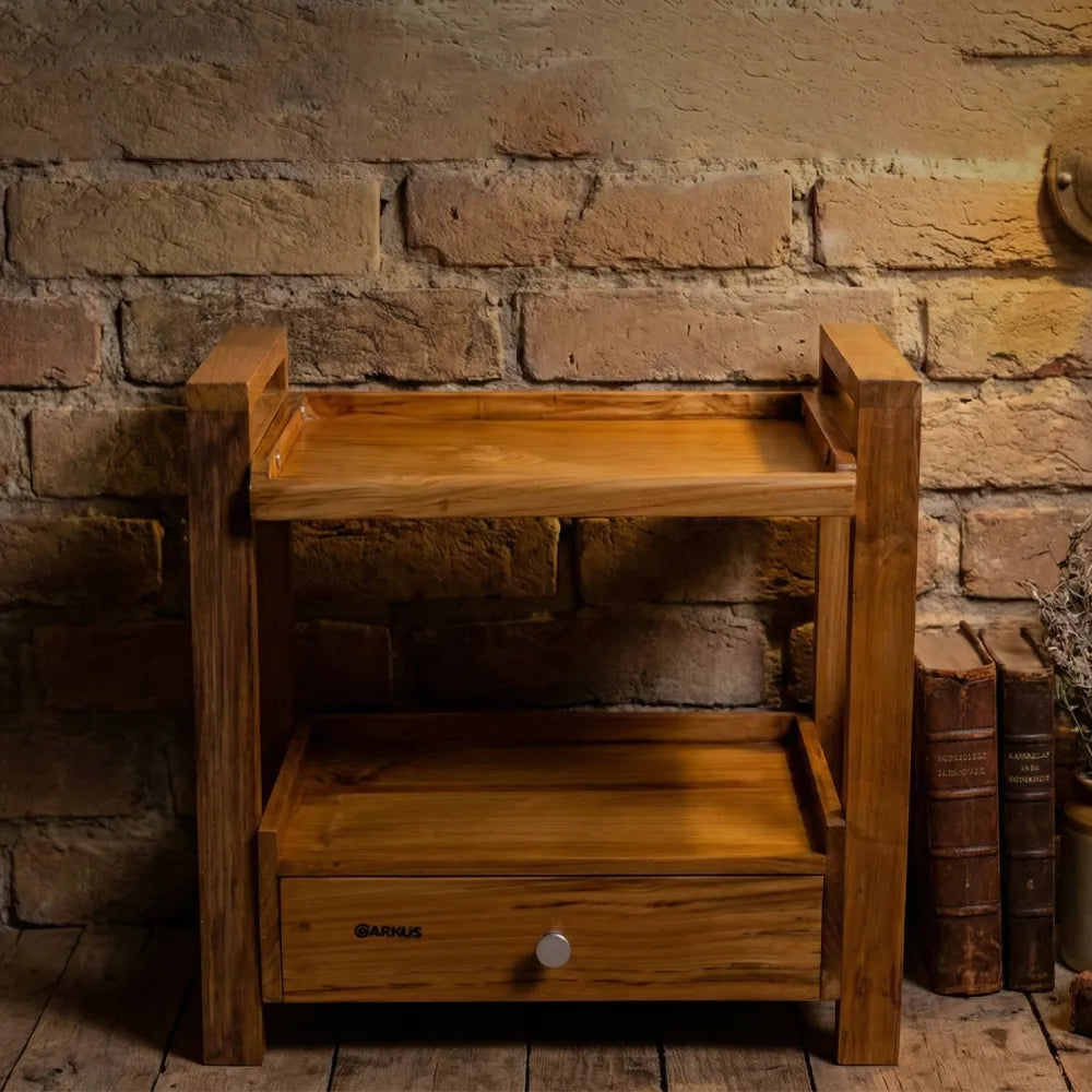 Wooden side table with a drawer against a brick wall.