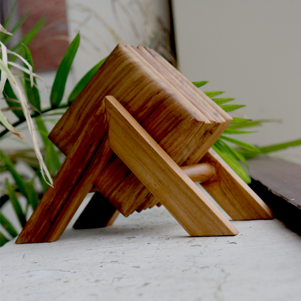 Wooden square tea coasters on a marble surface with plants in the background
