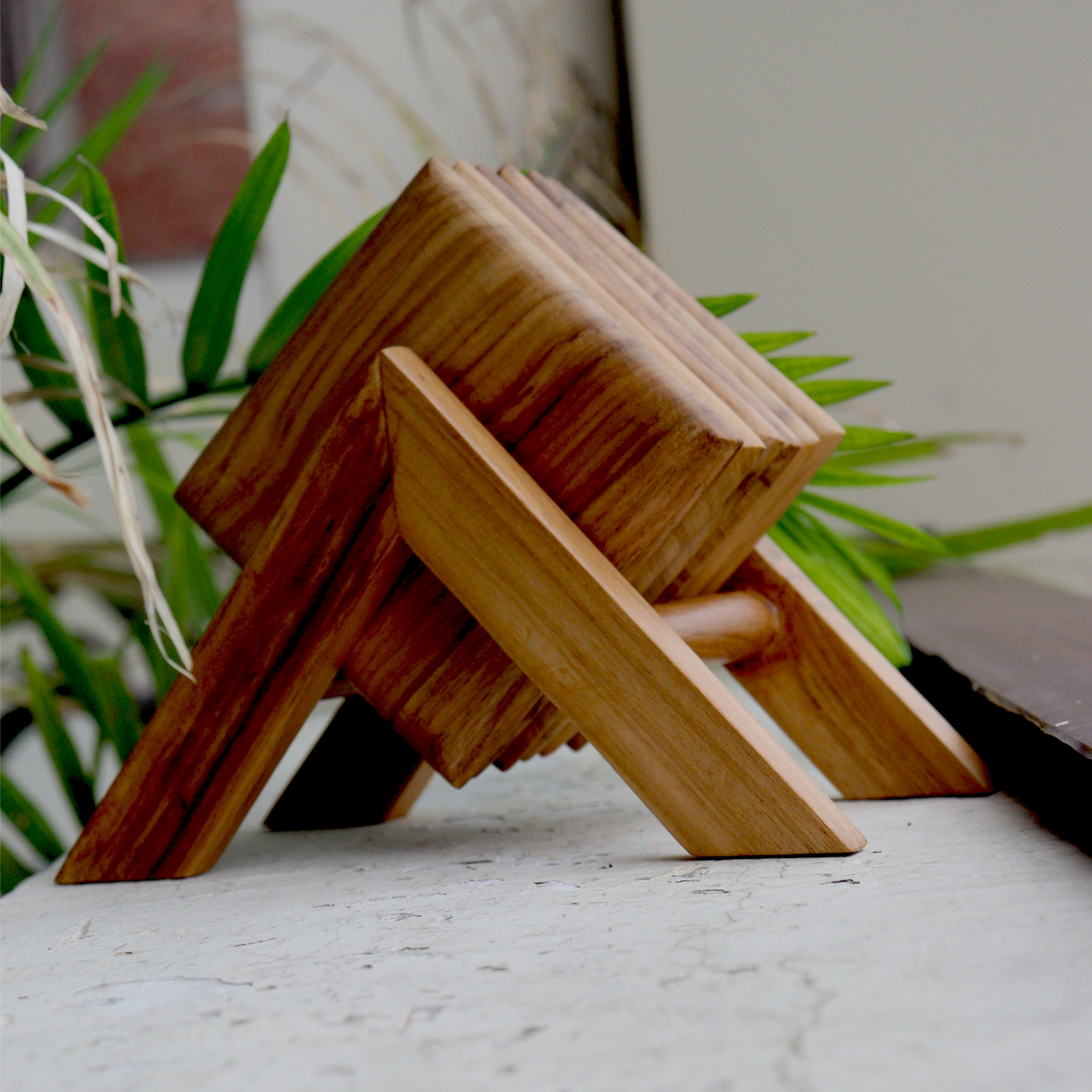 Wooden square tea coasters on a marble surface with plants in the background