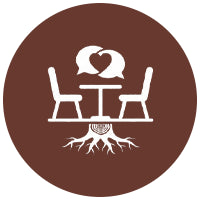 Icon of a two chairs at a table with a heart above, surrounded by tree roots, on a brown circle.