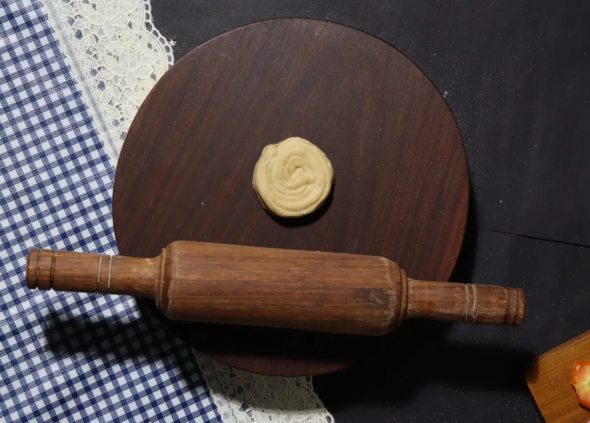 Wooden rolling pin on a dark surface with a small ball of dough.